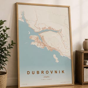 Può includere: Una stampa incorniciata di una mappa di Dubrovnik, Croazia, in una cornice di legno chiaro. La mappa presenta un design topografico nei toni del marrone e uno sfondo azzurro. La parola "DUBROVNIK" è stampata in marrone.