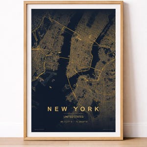 Op de afbeelding: Een ingelijste kaartprint van New York City, met een gedetailleerd goudkleurig stratenraster op een donkerblauwe achtergrond. De tekst "NEW YORK" en "UNITED STATES" is in goud. De lijst is gemaakt van lichtgekleurd hout.