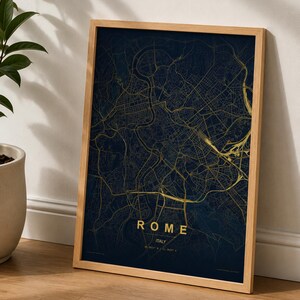 Puede incluir: Un mapa enmarcado de Roma, Italia, con un fondo azul oscuro y líneas de la ciudad doradas. La palabra "ROME" está impresa en dorado en la parte inferior, junto con el nombre del país y las coordenadas. El marco es de madera clara.