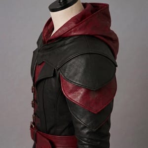 Shoulder view of a black and red genuine leather hooded coat with layered shoulders and adjustable metal buckles, designed for medieval Halloween LARP and dark fantasy cosplay.
