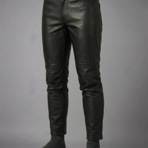 Puede incluir: Pantalones de cuero negro con acabado liso, cierre cl&aacute;sico de bot&oacute;n y cremallera, y costuras horizontales en la zona de las rodillas. Los pantalones tienen un corte ajustado con costuras visibles a lo largo de las piernas y bolsillos.