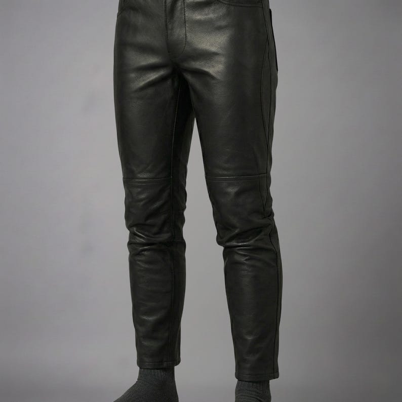 Puede incluir: Pantalones de cuero negro con acabado liso, cierre cl&aacute;sico de bot&oacute;n y cremallera, y costuras horizontales en la zona de las rodillas. Los pantalones tienen un corte ajustado con costuras visibles a lo largo de las piernas y bolsillos.
