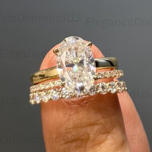 May include: A three-piece diamond ring set. The engagement ring features a large oval-cut diamond, flanked by two bands, one with small diamonds. The rings are set in gold. The brand name "EleganceDiamondUS" is visible.
