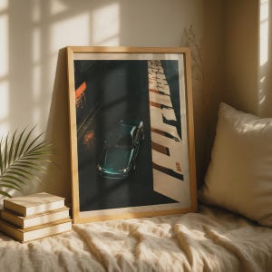 May include: A framed vertical art print featuring a dark green sports car viewed from above on a dark asphalt road. A large, bright white rectangular light beam illuminates the right side of the composition, casting a long shadow across the dark surface.