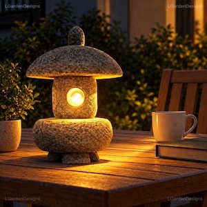 May include: A grey stone lantern with a mushroom-shaped top and a central circular opening emitting a warm, glowing light. The lantern features a textured, speckled surface and rests on a sturdy base, providing illumination in a dark setting.