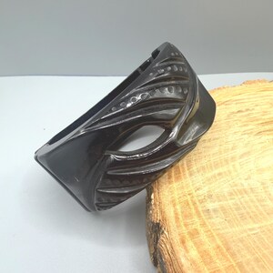 May include: A black, carved bangle bracelet with a geometric design. The bracelet has a glossy finish and features carved lines and dotted patterns. The design is angular and modern, suitable for everyday wear.