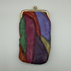 Puede incluir: Un monedero de cuero de retazos de colores con un cierre dorado. El monedero presenta una variedad de colores, incluyendo rojo, verde, morado y amarillo, cosidos con hilo negro. La forma rectangular es ideal para llevar objetos pequeños.