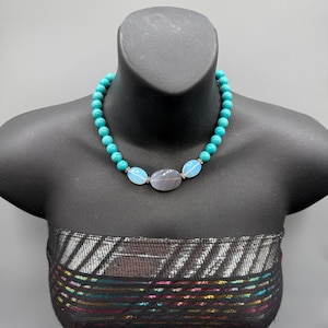 May include: A white ceramic mug with a black handle and the text "But First, Coffee" in a bold, black font. The mug is set against a blurred background, suggesting a cozy setting.