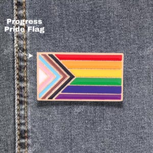 May include: A rectangular Progress Pride Flag pin with a gold border. The flag features a rainbow design with additional colors representing inclusivity. The text "Progress Pride Flag" is visible in the upper left corner.