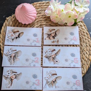 Op de afbeelding: Zes rechthoekige kaarten met illustraties van een vrouw met een breedgerande hoed versierd met bloemen. Elke kaart heeft een ander roze nummer. Een roze decoratief item en bloemen staan ook in de afbeelding.
