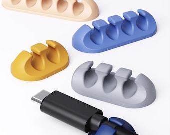 May include: A collection of cable organizers in various colors: beige, blue, yellow, and gray. Each organizer has multiple slots to hold cables. A black USB-C cable is shown inserted into a blue organizer, demonstrating its use.