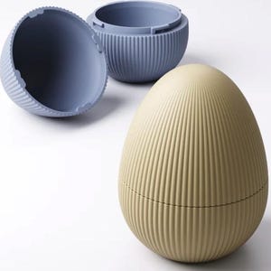 Può includere: Tre contenitori a forma di uovo. Uno è aperto, rivelando l'interno. I contenitori sono a coste e nelle tonalità del blu e del beige. I contenitori a forma di uovo sono su sfondo bianco.