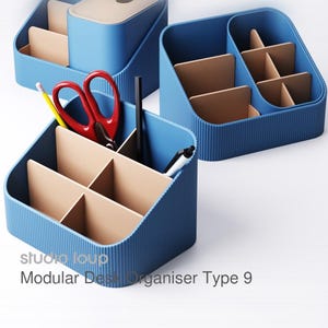 Könnte beinhalten: Blaue modulare Schreibtisch-Organizer mit beigen Trennwänden. Ein Organizer enthält rote Scheren, einen gelben Bleistift und schwarze Stifte. Der Text "studio loup Modular Desk Organiser Type 9" ist sichtbar.