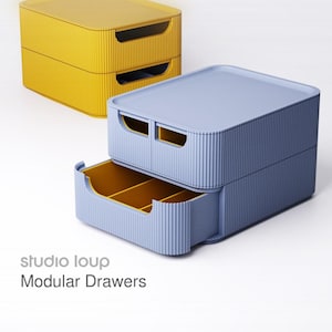 Könnte beinhalten: Zwei modulare Schubladeneinheiten, eine gelbe und eine blaue. Die blaue Einheit hat eine offene Schublade, die ein gelbes Innere mit Trennwänden zeigt. Der Text "studio loup Modular Drawers" ist sichtbar.