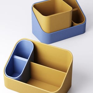 Pode incluir: Organizadores de secretária bicolores em azul e amarelo. Os organizadores têm uma textura canelada no exterior e apresentam vários compartimentos para canetas, lápis e outros materiais de escritório. O design é moderno e minimalista.