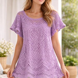 May include: A lilac crochet top with short, flared sleeves. The top has a delicate open-weave design and a scalloped hemline. The round neckline is also open-weave. The top is worn with white shorts.