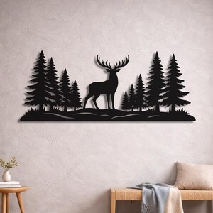 Könnte beinhalten: Schwarze Metall-Wandkunst, die einen Hirsch zwischen Kiefern zeigt. Das Silhouette-Design zeigt einen Hirsch mit großem Geweih und detaillierten immergrünen Bäumen, wodurch eine von der Natur inspirierte Szene entsteht. Das Kunstwerk ist an einer hellen Wand befestigt.