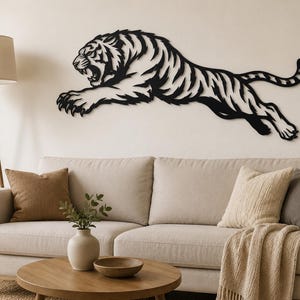 Op de afbeelding: Een zwart metalen wanddecoratie die een tijger in een dynamische spronghouding weergeeft met de bek open en de klauwen uitgestrekt. Het silhouet bevat ingewikkelde uitgesneden details die de strepen en de gespierde vorm van de tijger weergeven.