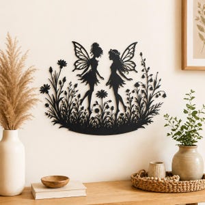 Peut inclure: Décoration murale en métal noir représentant deux fées aux ailes détaillées, dans un champ de fleurs et de feuillage. Les silhouettes sont finement découpées, créant une pièce fantaisiste et décorative pour la décoration intérieure.