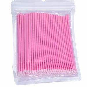 Op de afbeelding: Een doorzichtige plastic zak gevuld met talrijke roze micro-applicators. Elke applicator heeft een dunne, roze steel en een witte, wattenachtige punt. De applicators zijn netjes gerangschikt in de zak.