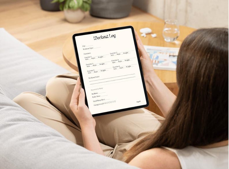 May include: A black tablet displaying a "Workout Log" template. The template includes sections for date, workout type, exercises, sets, reps, weight, and notes. The tablet is held by a person.