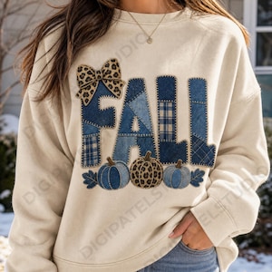 Puede incluir: Una sudadera de cuello redondo color crema con la palabra FALL en letras grandes estilo patchwork hechas de tela de mezclilla azul y cuadros. Un lazo con estampado de leopardo se sitúa sobre las letras y tres calabazas con patrones de mezclilla y leopardo debajo.