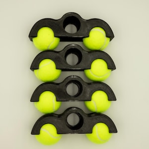 May include: Four black tennis ball holders, each holding two yellow tennis balls. The holders are stacked vertically, with a circular hole in the centre of each. The tennis balls are bright yellow.