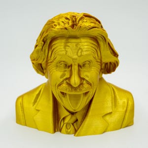 May include: A gold-colored bust of Albert Einstein, featuring his iconic hairstyle, mustache, and a suit jacket. The sculpture has a detailed texture and a smiling expression.