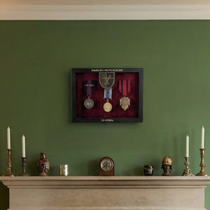 May include: A living room featuring a fireplace with a burning fire, flanked by armchairs and lamps. Above the fireplace is a display case containing medals. The walls are painted a rich green, and the room is decorated with candles and artwork.