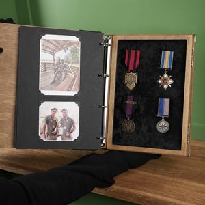May include: A wooden display case with a black interior, showcasing military medals and two framed photographs. The medals feature red, blue, and purple ribbons. The photographs depict two men in uniform.