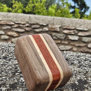 May include: A rectangular wooden block featuring a dark brown walnut exterior, a central reddish-brown wood stripe, and two thin light-colored wood accents separating the sections. The object has rounded edges and a smooth, polished finish.
