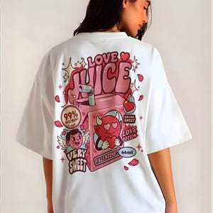 May include: White t-shirt with a colourful graphic design on the back. The design features a pink juice box with the words "LOVE JUICE" and "VALENTINE" along with cartoon characters and hearts. The shirt also has the text "VERY SWEET" and "DRINK SWEET LOVE POTION".