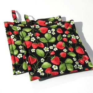 May include: Two black quilted pot holders with a strawberry print. The pot holders have a loop handle.