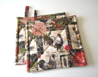 May include: Two quilted pot holders with a rooster and floral design. The fabric features roosters, red flowers, and green leaves on a cream and black background. Each pot holder has a fabric loop for hanging.