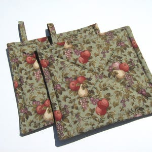 May include: Two green quilted pot holders with a floral pattern featuring apples, pears, and grapes. The pot holders have a loop for hanging.