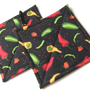 May include: Two black quilted hot pads with a chili pepper and green pepper print. The hot pads are square and have a black background with red, green, and yellow chili peppers and green peppers.