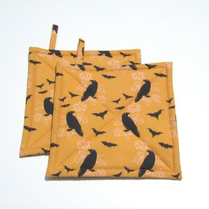 May include: Two yellow quilted pot holders with a black raven and bat pattern.