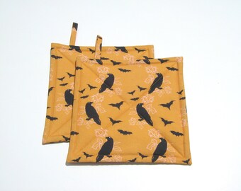 May include: Two yellow quilted pot holders with a black raven and bat pattern.