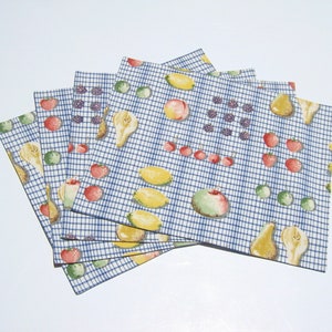 May include: A stack of four rectangular placemats with a blue and white checkered pattern. Each placemat is decorated with illustrations of various fruits, including pears, lemons, apples, strawberries, and blackberries. The placemats are arranged in a fan shape.