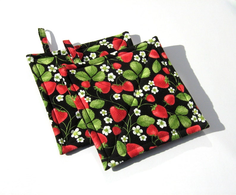 May include: Three black quilted pot holders with a strawberry print. The pot holders have a loop handle for easy grabbing.