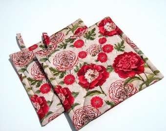 May include: Two quilted pot holders with a floral pattern. The pot holders are beige with red and white flowers. The flowers are a peony design.