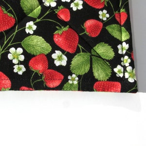 May include: Black fabric with a repeating pattern of red strawberries and white flowers. The fabric has a stitched edge.