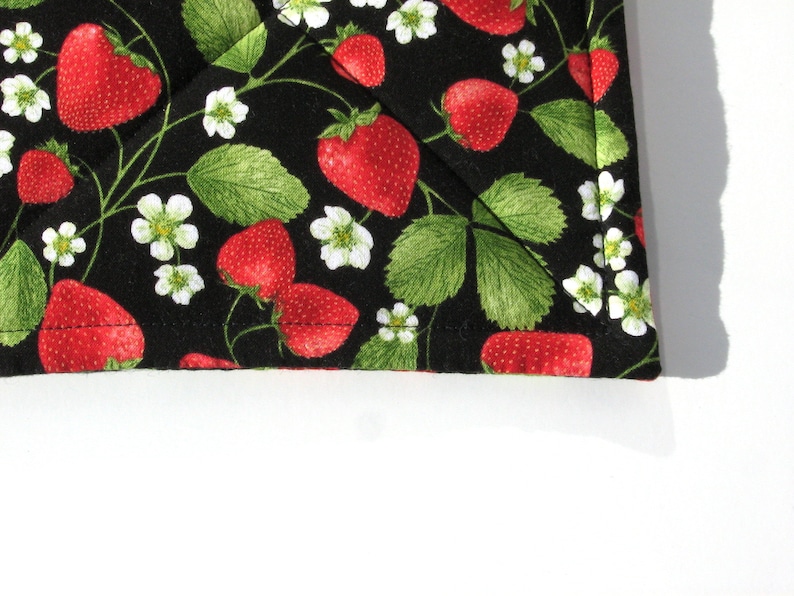 May include: Black fabric with a repeating pattern of red strawberries and white flowers. The fabric has a stitched edge.