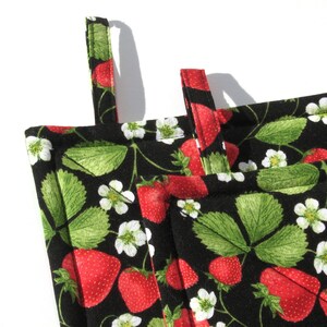 May include: Black and white pot holder with a strawberry print. The pot holder has two loops for hanging and is made of fabric.