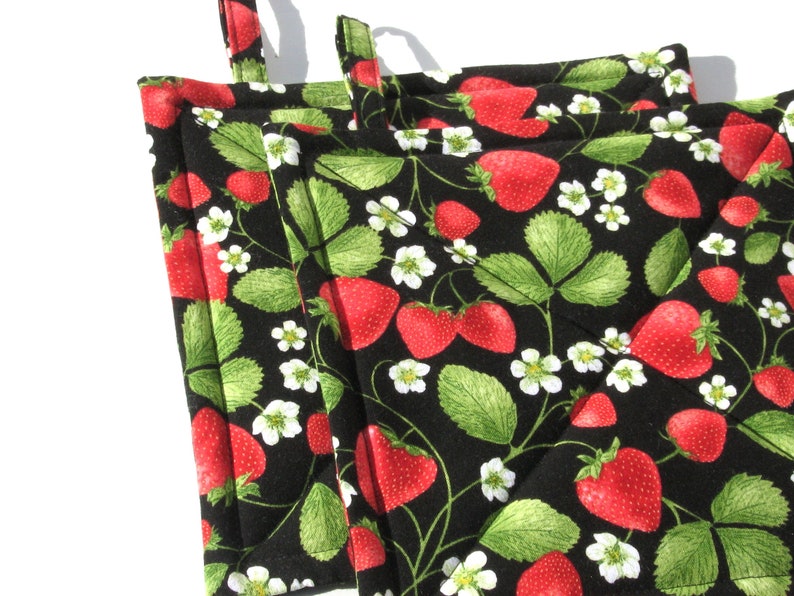 May include: Set of four black quilted pot holders with a strawberry and leaf design. The pot holders are red and green.