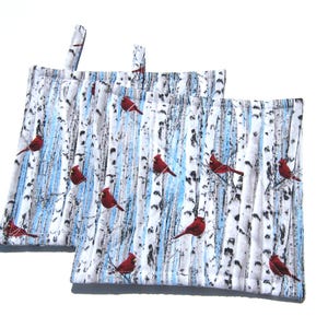 May include: Two quilted pot holders with a wintery birch tree and cardinal design. The pot holders are white with blue and gray birch trees and red cardinals.