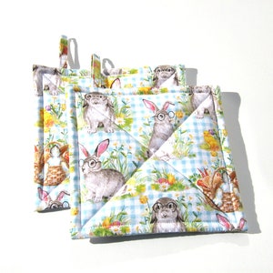 May include: Set of three blue and white quilted pot holders with a bunny rabbit and chick pattern. The pot holders are square and have a loop for hanging.