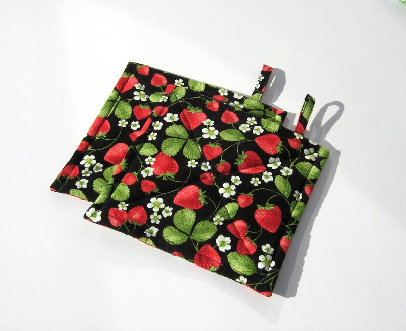 May include: Two black quilted pot holders with a strawberry print. The pot holders have a hanging loop.
