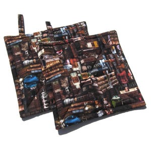 May include: Two brown and black pot holders with a vintage book and bottle print. The pot holders have a loop handle.