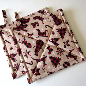 May include: Two quilted pot holders with a Christmas theme. The fabric is beige with red and black buffalo plaid and white snowflakes. The design includes a reindeer, a Christmas tree, a snowman, an angel, a sleigh, and a candy cane.